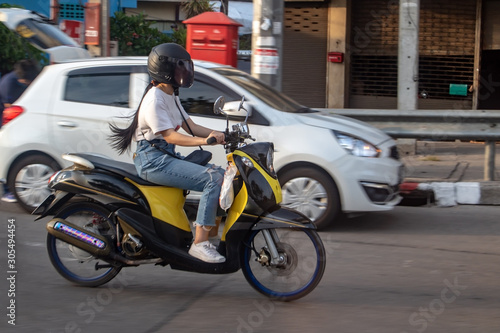 A young woman riding a motorcycle on road. Asian girl rides scooter in the city street  Samut Prakan  Thailand.