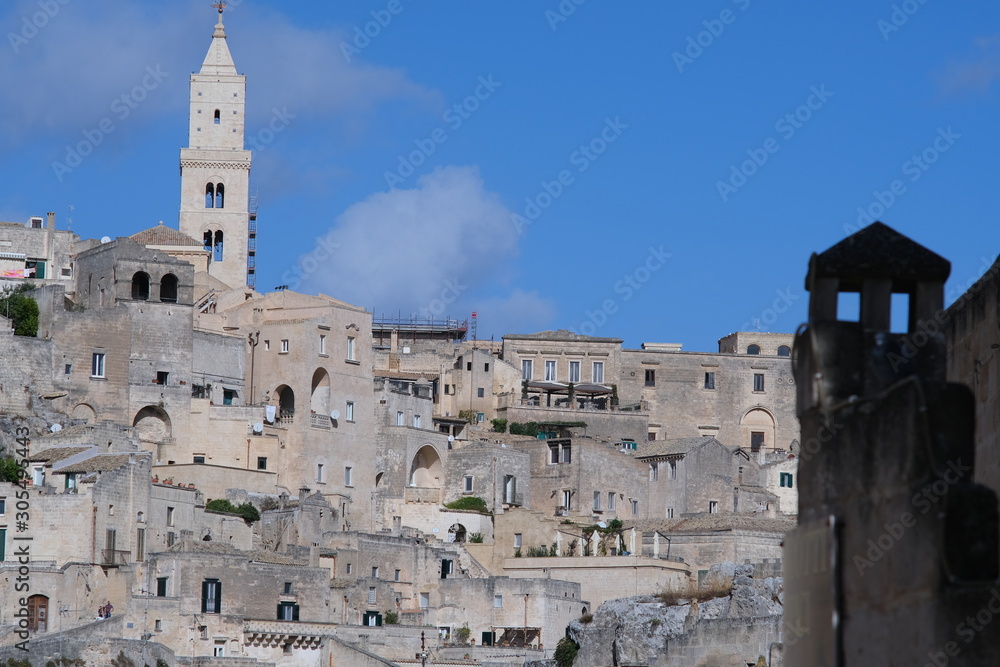 Panorama of houses and of the Sassi of Matera with roofs and streets. Blue sky with church and bell tower with blue sky background with clouds.