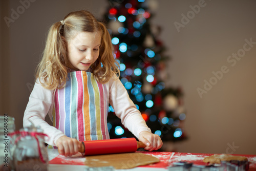 Pretty little girl decoraiting christmas cookies at home with christmas tree on background photo