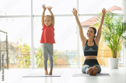 Young woman and her daughter doing exercise indoors. Home fitness