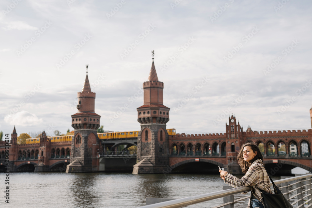 Smiling woman with smartphone in the city at Oberbaum Bridge, Berlin, Germany Smiling woman with smartphone in the city at Oberbaum Bridge, Berlin, Germany