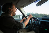 Side view photo of adult middle aged male with long dark hair driving his truck car through nature scenes while yawning and being very tired 