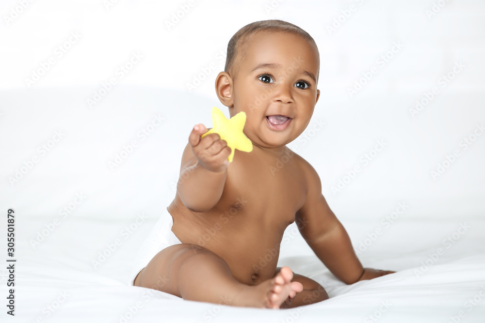 American baby girl sitting on white bed and holding yellow toy American baby girl sitting on white bed and holding yellow toy