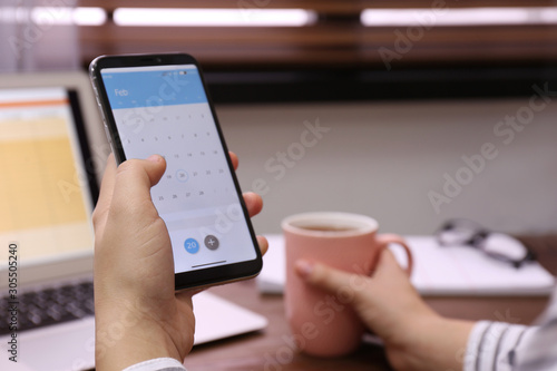 Woman holding smartphone with calendar app at table, closeup
