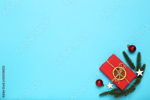 Flat lay christmas composition. Gift box with baubles and fir tree branches on blue background