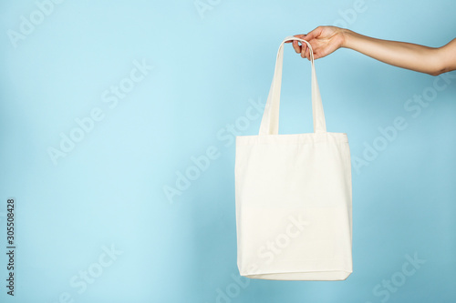 Female hand holding white cotton eco bag on blue background
