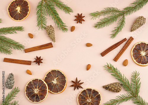 Christmas composition on a pink background. Cinnamon, anise, almonds, cones, slices of orange, spruce branches occupy the entire space of the frame.