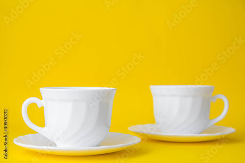 White ceramic cups with saucers on yellow background. White tableware crockery set. Space for text