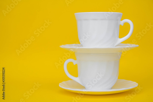 Fototapeta Naklejka Na Ścianę i Meble -  White ceramic cups with saucers on yellow background. White tableware crockery set. Space for text