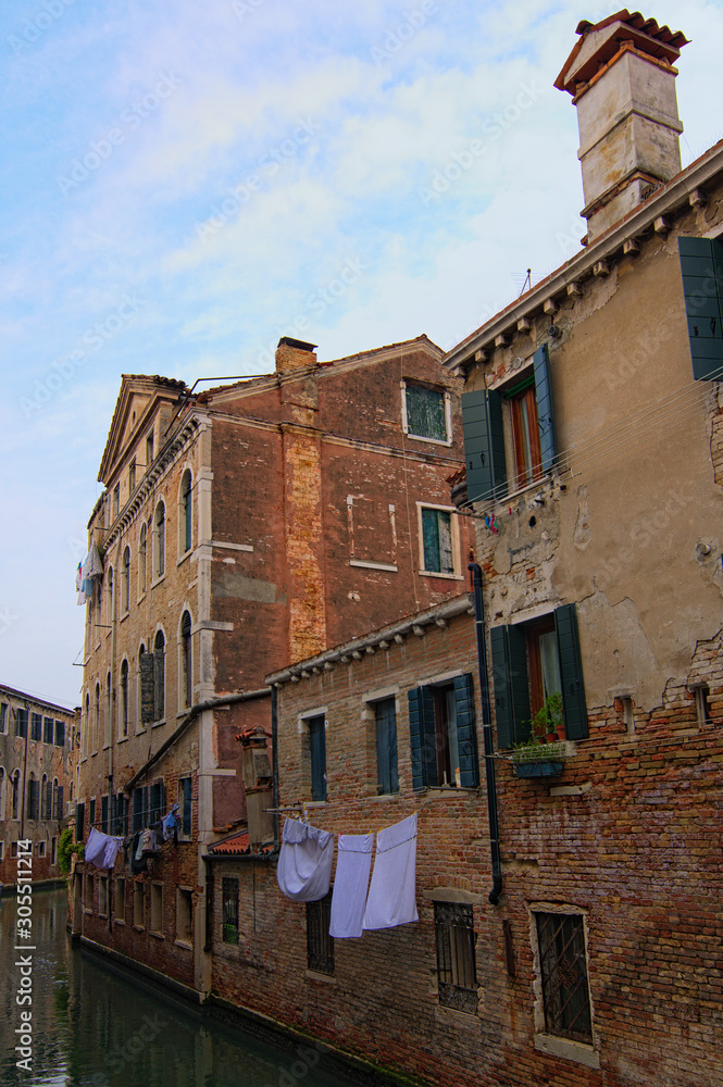 Medieval red brick buildings in Venice reflected in turquoise water. The clothes are dried on a rope along the wall. Non-tourist part of the city. Shaming street in Venice, Italy