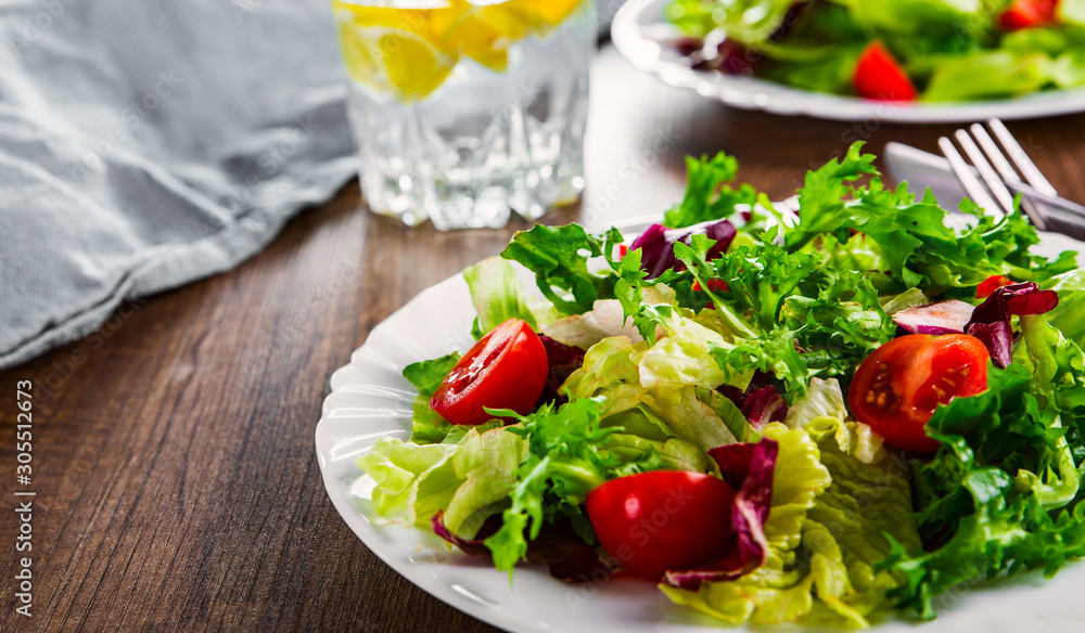 various fresh mix salad leaves with tomato in white plate on wooden background. various fresh mix salad leaves with tomato in white plate on wooden background.