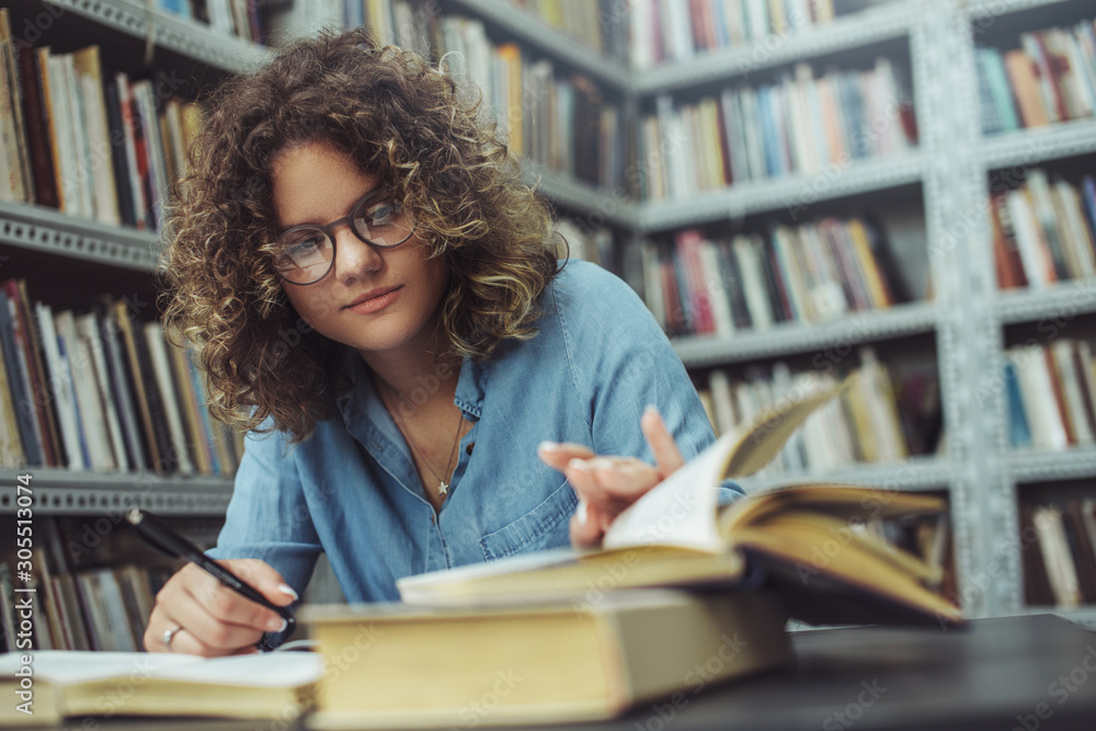 Young female student at the library. Young student reading book at library. Student learning for exam at library. Young female student at the library. Young student reading book at library. Student learning for exam at library.