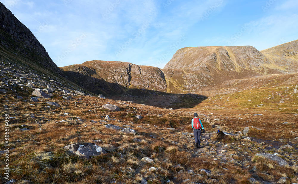 A hiker walking through Coire na Sleaghaich towards the summit of Slioch in the distance on bright sunny winters day in the Scottish Highlands.