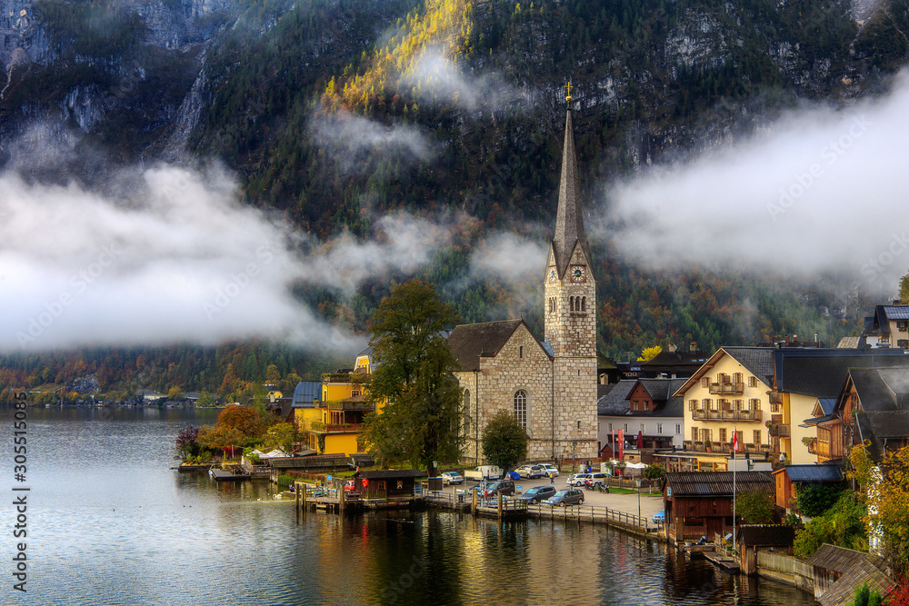 Fantastic Foggy Sunrise in the Mountains Lake. Classic postcard view of famous Hallstatt lakeside town in the Alps a beautiful Warm sunny morning with fog and clouds in autumn, Salzkammergut, Austria.