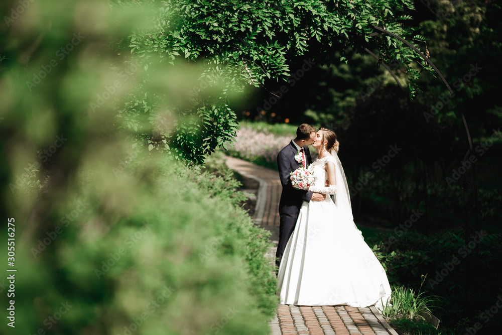 Beautiful bride and groom embracing and kissing on their wedding day outdoors Beautiful bride and groom embracing and kissing on their wedding day outdoors