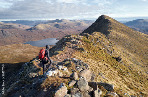 A hiker walking over the narrow ridge that leads to Sgurr an Tuill Bhain with Lochan Fada in the distance in the Scottish Highlands. photo