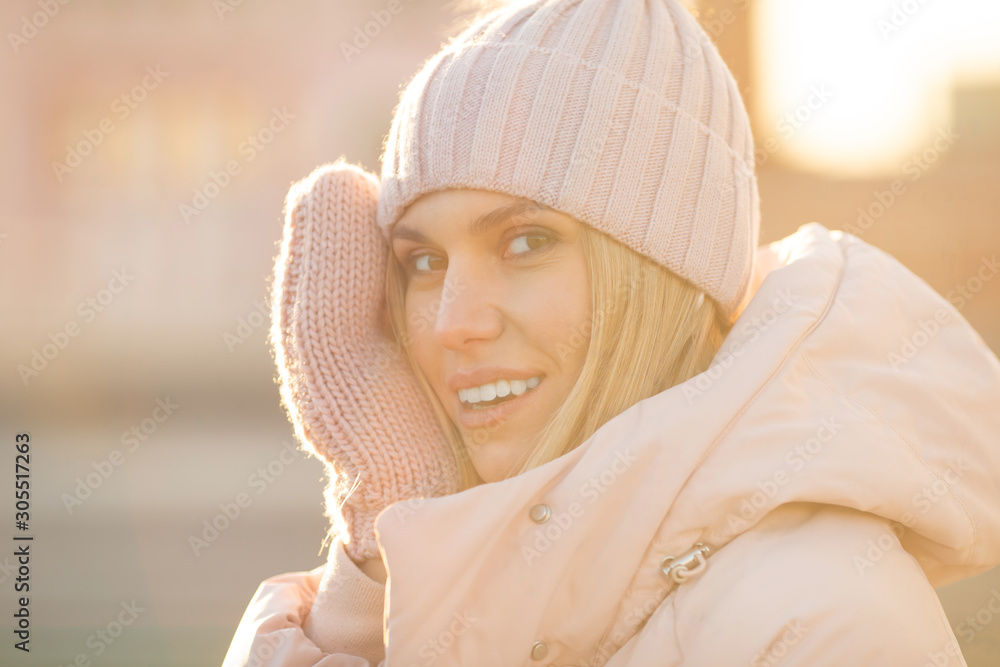 Obraz premium Portrait of a beautiful young model in pink knitted hat and mittens. Beautiful natural young smiling blonde woman wearing knitted gloves.