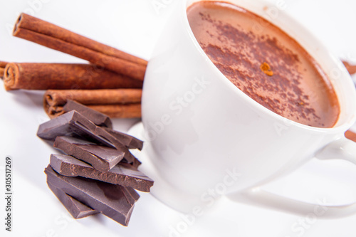 Cup of hot chocolate with cinnamon, and pieces of dark chocolate on a white background