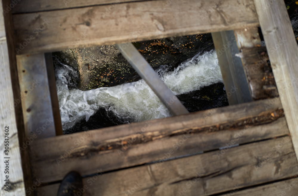 Looking down through a hole in a rotten wooden footbridge with the stream far below. Looking down through a hole in a rotten wooden footbridge with the stream far below.
