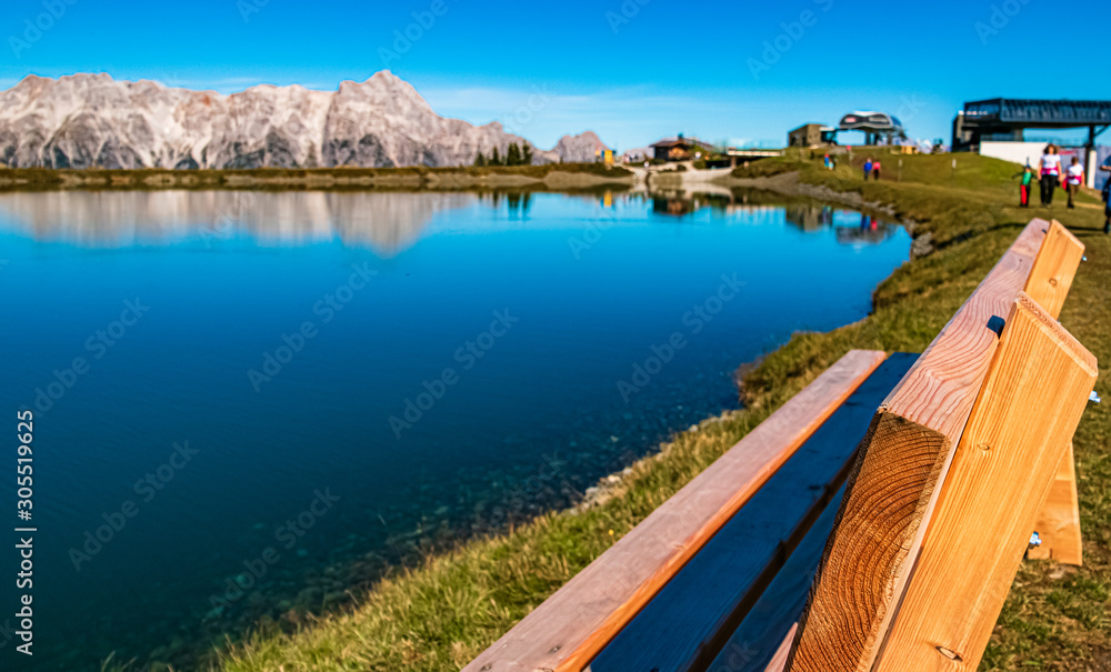 Beautiful alpine view with reflections in a lake and details of a bench at Leogang, Salzburg, Austria