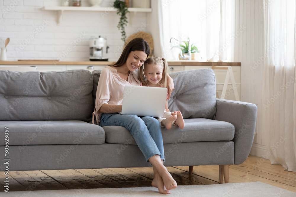 Loving mom teaching child daughter using laptop sit on sofa Loving mom teaching child daughter using laptop sit on sofa
