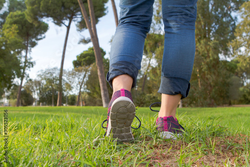 Woman with sneakers and jeans walking on grass.