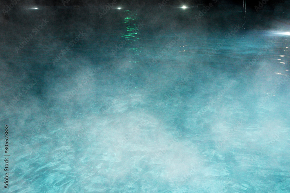 Pure clear water in the thermal pool. Hot water flows, and fog rises above the pool, the pool itself is illuminated by lanterns. Blue water, beautiful background.