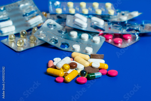 Close-up of assorted multi-colored pills on a blue background. Medical flat lay.