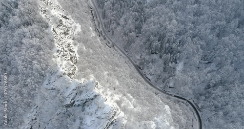Aerial view of mountain road in winter time. Sunlit cliffs and snow covered forest