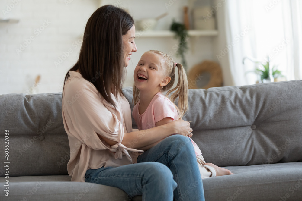 Cheerful mom playing laughing with adorable little daughter on sofa