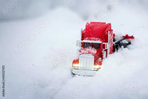 Toy red truck brings New Year and Christmas gifts. Winter holidays are coming. He rides through real snowdrifts. Winter shooting on the street. Headlights is on