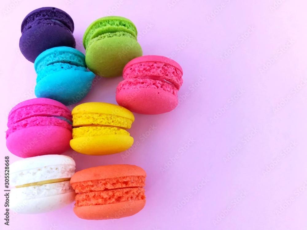 Fototapeta premium Delicious macaron sweets arranged on left,&nbsp; colorful macaroon on pink background