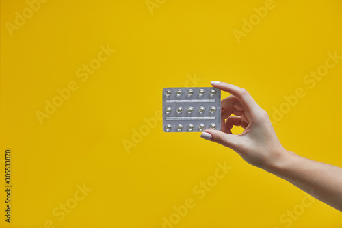 Obraz na plátně Female hand holding pills in blister pack on a yellow background
