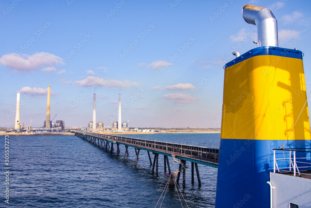 Coal ship funnel with a long industrial pier and a Coal and Gas fired power station including a Flue-Gas chimney in the background.