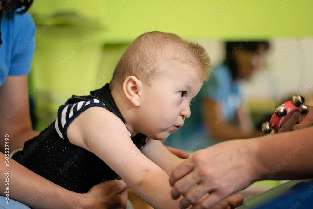 Portrait of a baby with cerebral palsy on physiotherapy in a children therapy center. Boy with disability has therapy by doing exercises. Little kid has musculoskeletal therapy in rehabitation centre. Portrait of a baby with cerebral palsy on physiotherapy in a children therapy center. Boy with disability has therapy by doing exercises. Little kid has musculoskeletal therapy in rehabitation centre.