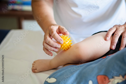 Baby having foot massage in a rehabilitation center. Little child on therapy. Massage therapist massaging a baby with yellow massage ball. photo