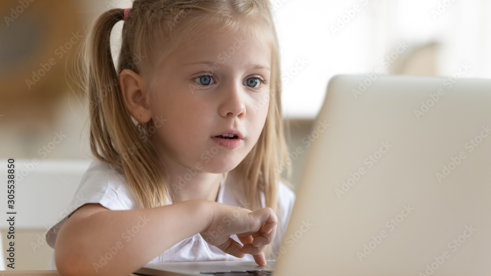 Curious surprised little kid girl using laptop alone at home Curious surprised little kid girl using laptop alone at home