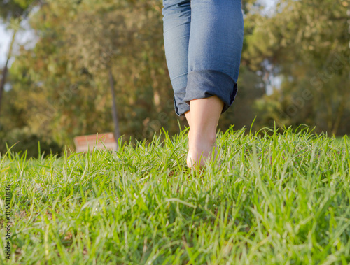 Woman with barefoots and jeans walking on grass.