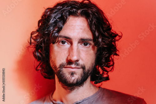 handsome italian young man with long, wavy hair, brown eyes,sad look and an orange background