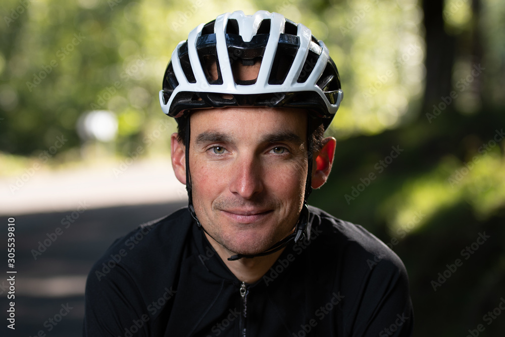 Confident adult man in bike helmet smiling and looking at camera on blurred background of park during training Confident adult man in bike helmet smiling and looking at camera on blurred background of park during training