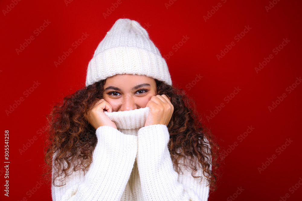 Studio portrait of young woman with dark skin and long curly hair wearing knitted turtle neck sweater over the festive red wall with a lot of copy space for text. Close up, isolated background.