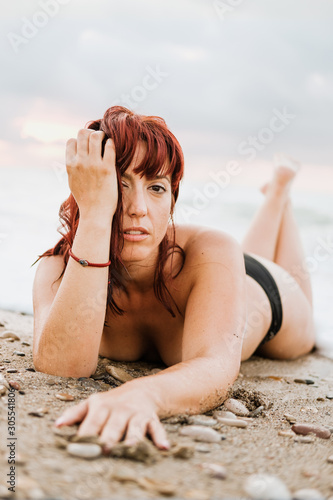 Young nude free calm female posing looking at camera while lying down in a rocky beach