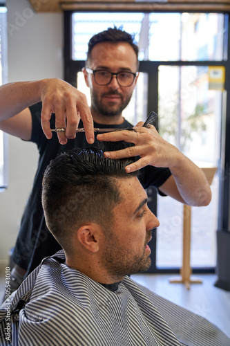 Stock vertical photo of a barber cutting hair with scissors and a comb to a customer. Design and style