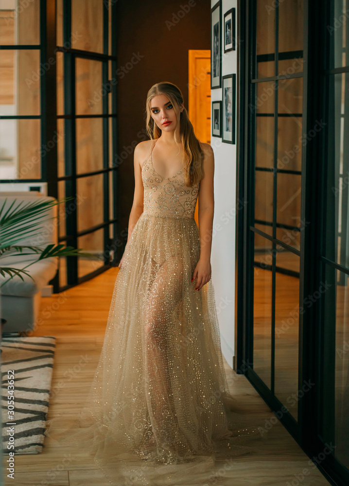 Stylish glamorous blonde woman in luxurious sparkling gold transparent dress.  Fashion style. Luxurious image for party. Evening outfit for the  graduation, Christmas, New Year. Background interior loft Stock Photo