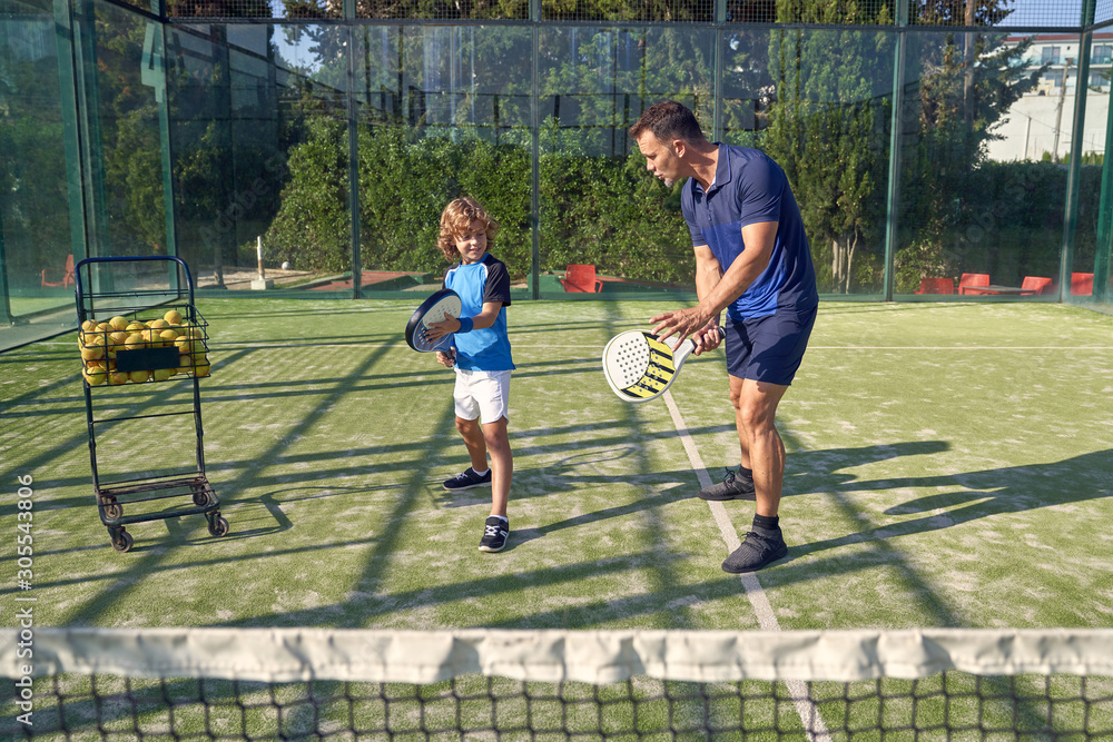 © PHILIPPE DEGROOTE/ADDICTIVE STOCK - Adult man showing boy how to hold paddle and hit ball during tennis training on sunny day on court © PHILIPPE DEGROOTE/ADDICTIVE STOCK - Adult man showing boy how to hold paddle and hit ball during tennis training on sunny day on court