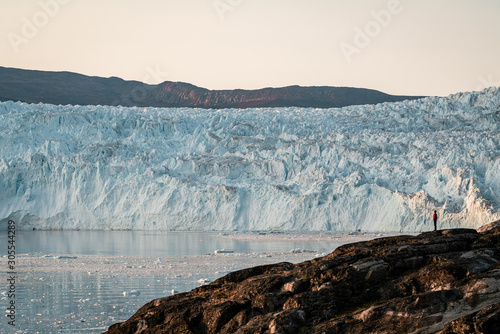 People sitting standing in front of huge glacier wall of ice. Eqip Sermia Glacier Eqi glacier in Greenland called the calving glacier during midnight sun. Hikers during travel and vacation. photo