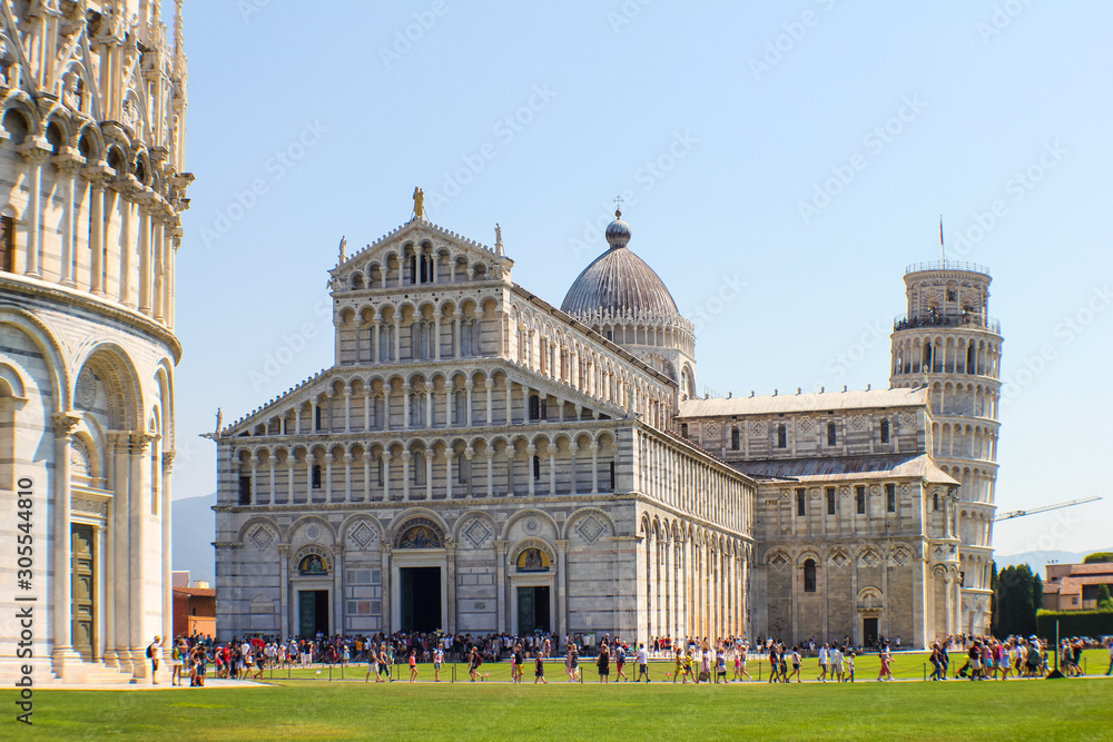 view of the baptistery of Pisa and behind the cathedral and the tower during a sunny day
