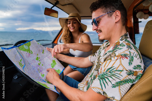 Side view of active smiling man in sunglasses looking at open road map and finding route with woman in hat in car