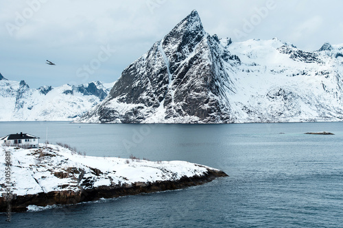 View of a landscape of a Norwegian fjord with a snowy mountain. In the foreground, on the rock is a small white house. Norway, Lofoten Islands photo