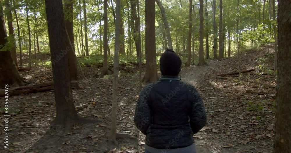 First person view following a man walking through a shaded forest First person view following a man walking through a shaded forest